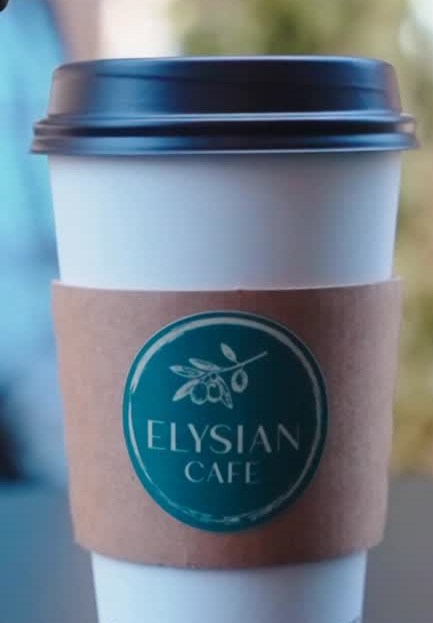 An Elysian Cafe coffee to-go with the green olive-branch logo, in the afternoon light